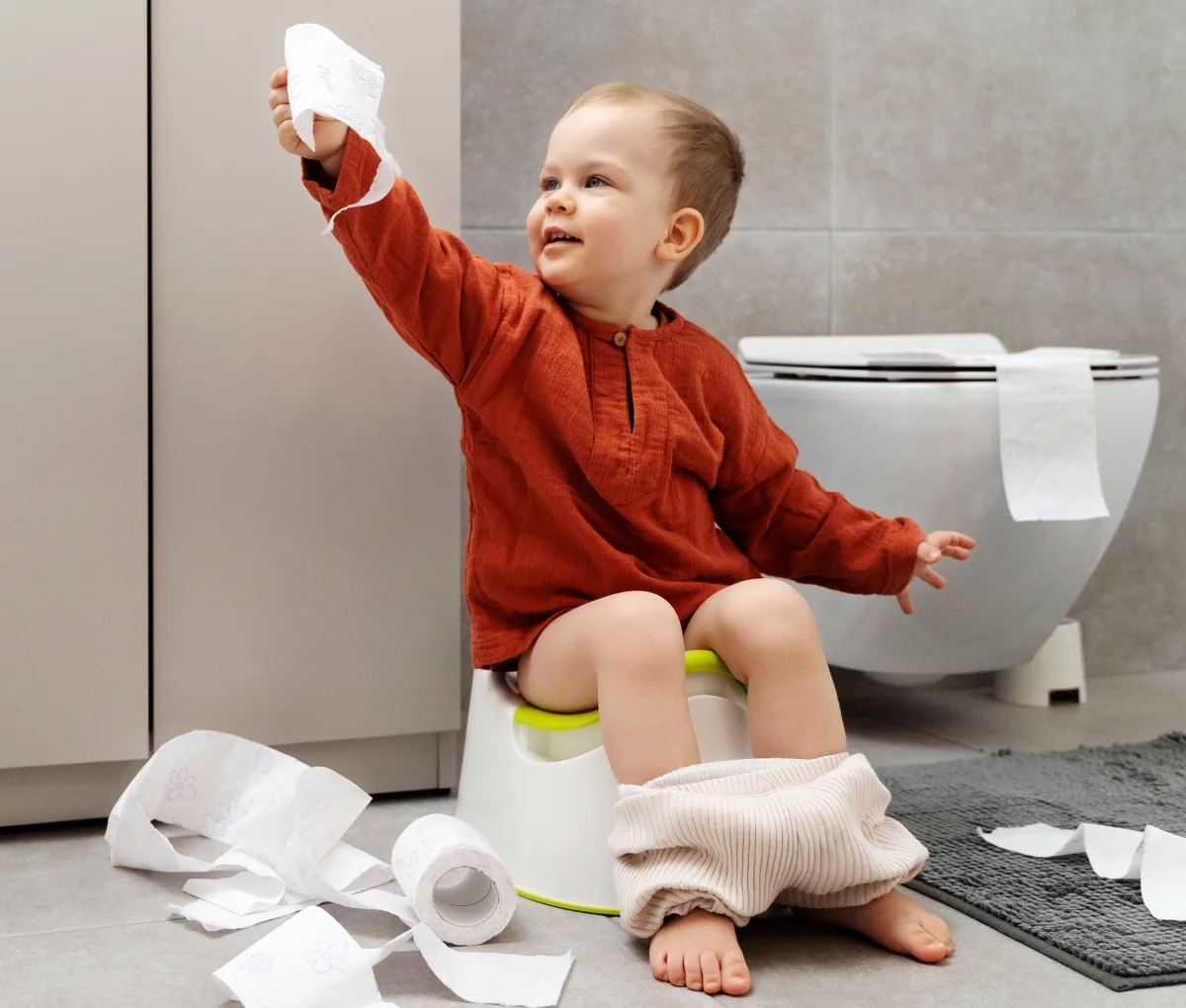 Toddler sitting on a potty and holding toilet paper